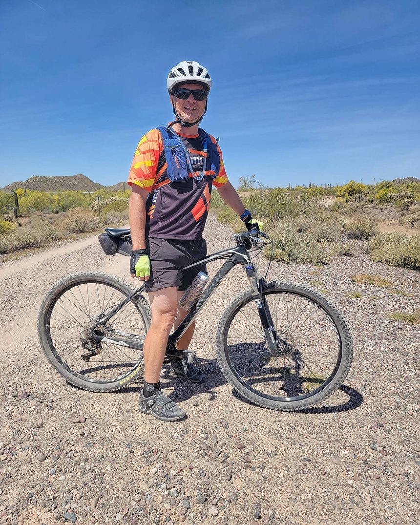 Daniel standing with his mountain bike on a desert trail under a clear blue sky