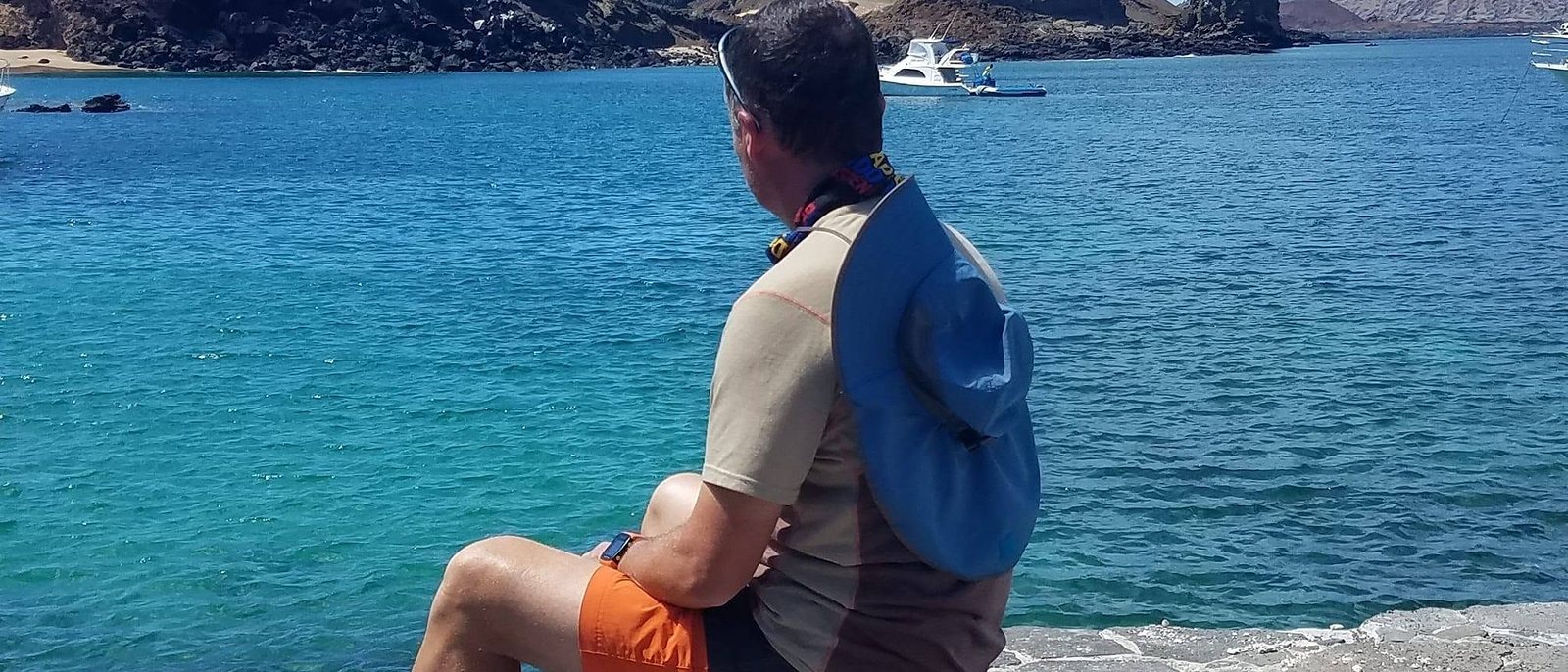 Daniel sitting alone on a rock ledge looking out over turquoise water and volcanic islands
