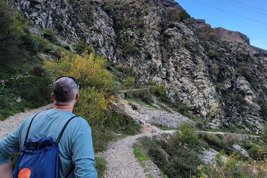 Daniel climbing a gravel trail toward a hilltop fortress