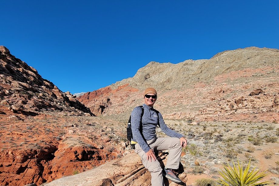 Daniel sitting on red sandstone looking out across desert peaks
