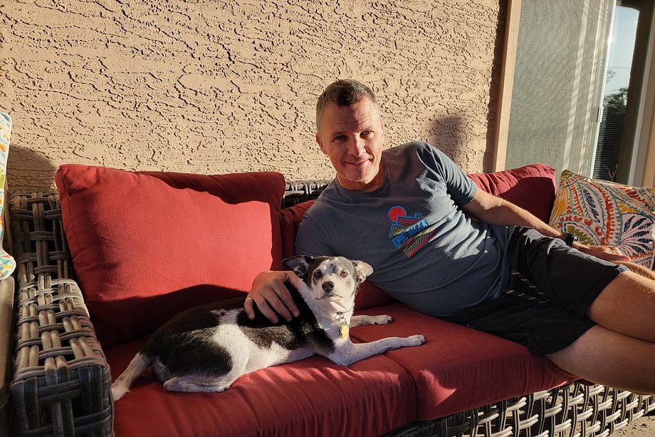 Daniel relaxing on a sofa at home with his dog beside him